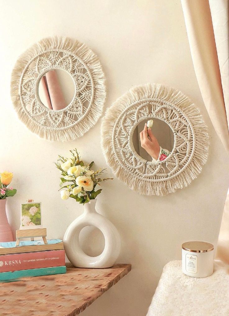 two circular mirrors hanging on the wall above a table with books and flowers in vases