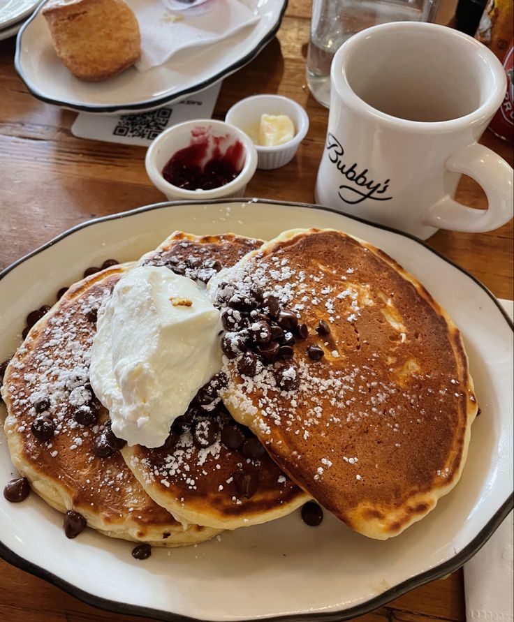 two pancakes on a plate with ice cream and chocolate chips next to coffee mugs