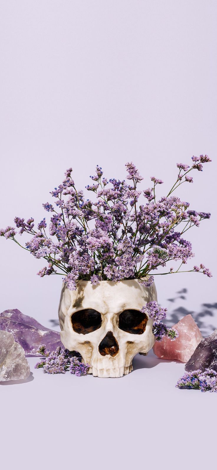 a skull vase filled with purple flowers on top of a white table next to crystals