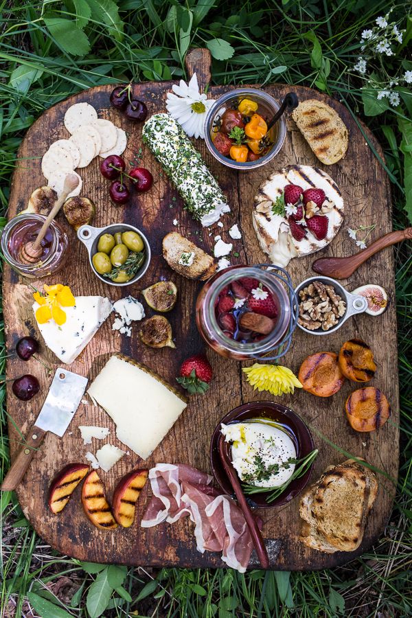 an assortment of cheeses, fruits and meats on a wooden platter in the grass