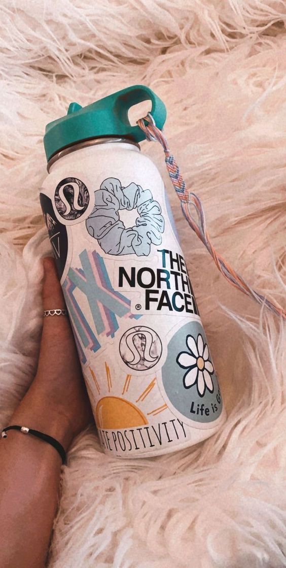 a person is holding a can of the north face water bottle on a furry surface