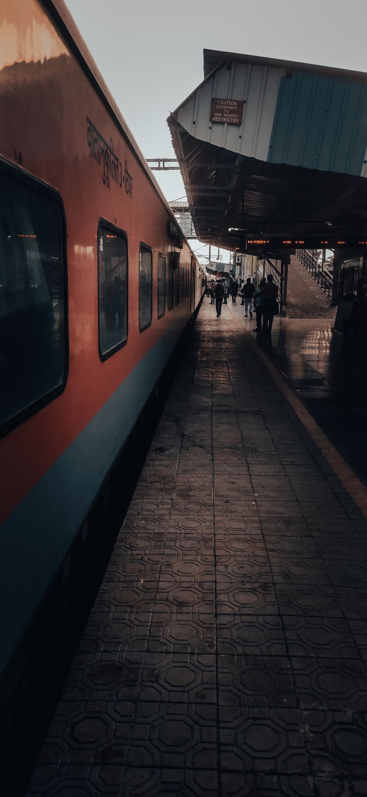 people are walking on the sidewalk next to a red and blue train at a station