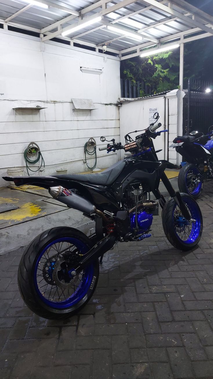 two motorcycles parked next to each other in a parking lot near a white building with blue trim