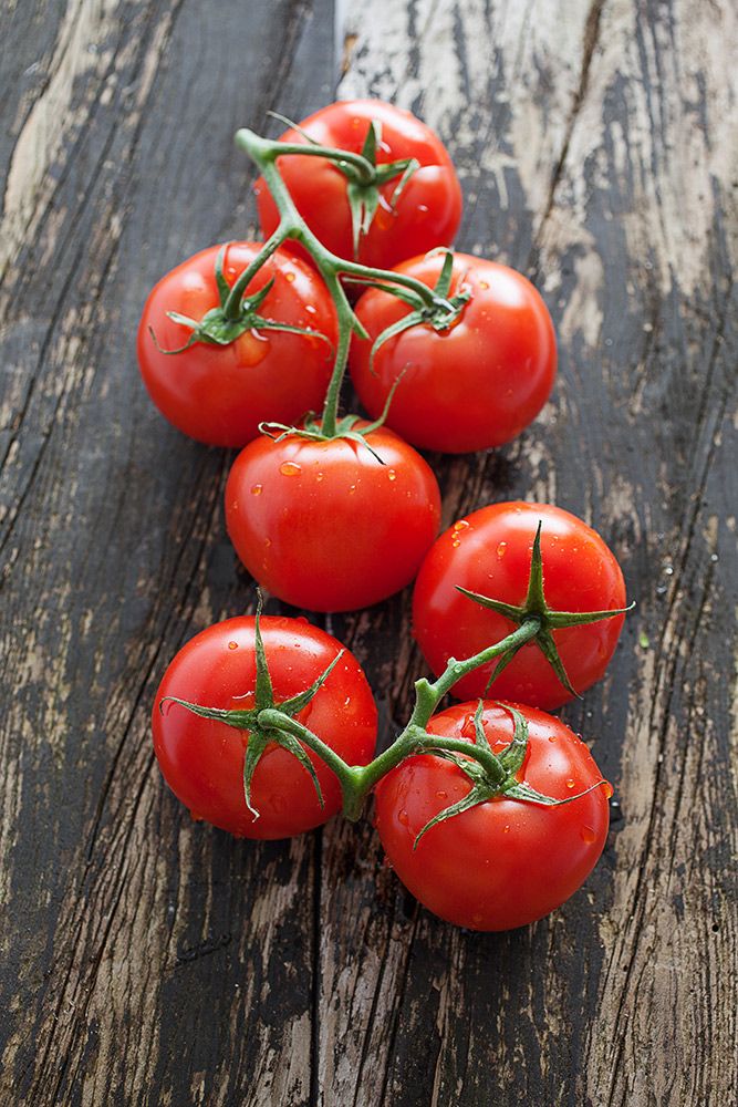 six tomatoes on a wooden table with green stems