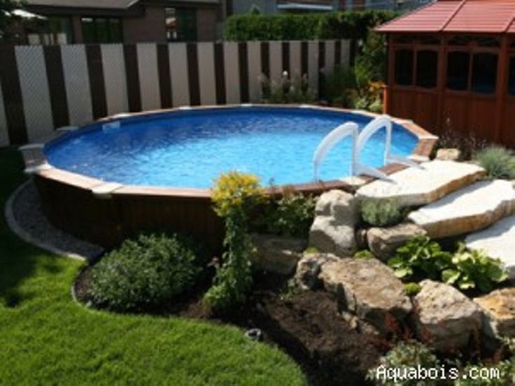 an above ground swimming pool surrounded by rocks and plants in a backyard with a wooden fence