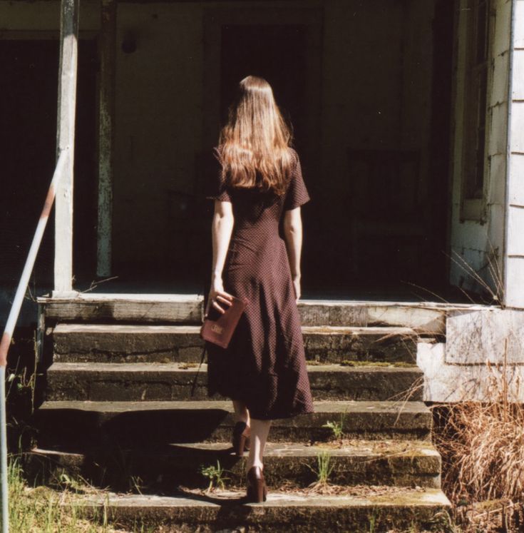 a woman in a brown dress is walking up some steps to a house with an open door