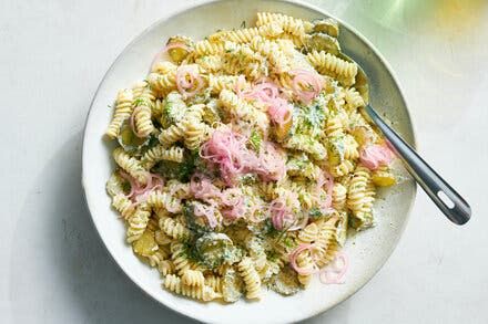 a white bowl filled with pasta salad on top of a table next to a fork