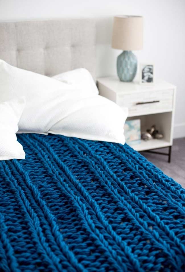 a bed with white pillows and blue knitted blanket