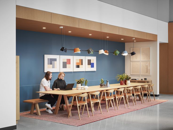 two women sitting at a long table with laptops on it in an office setting