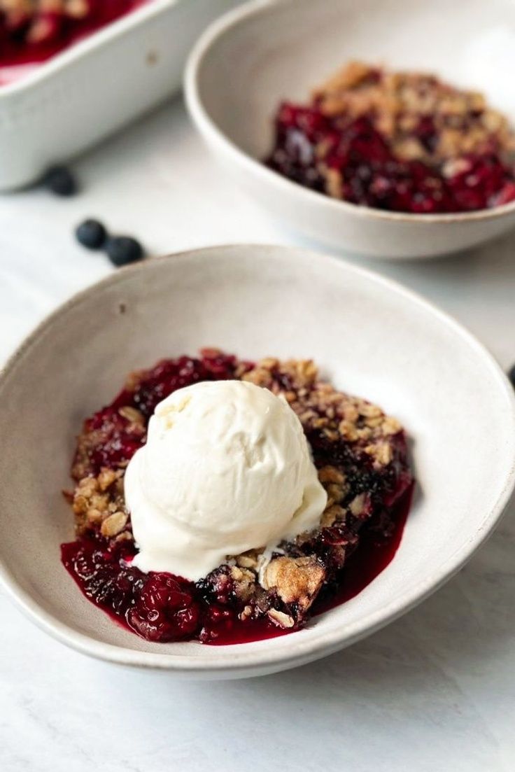 two white bowls filled with fruit and ice cream on top of a table next to blueberries