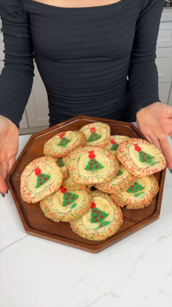 a woman holding a plate with christmas cookies on it