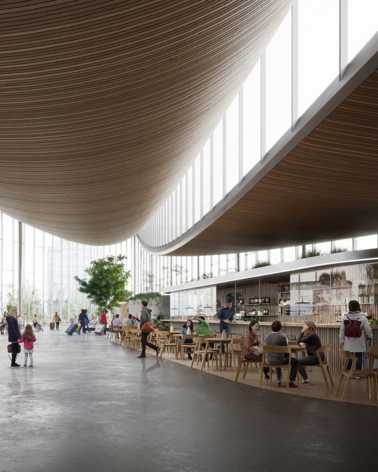 people are sitting at tables in an open area with large windows on the side of the building