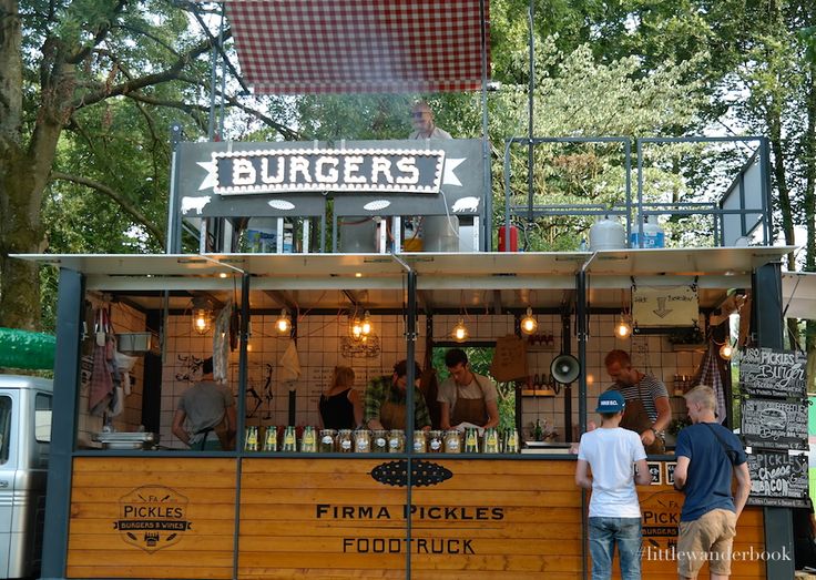 some people are standing at a food truck that is selling burgers and beer bottles