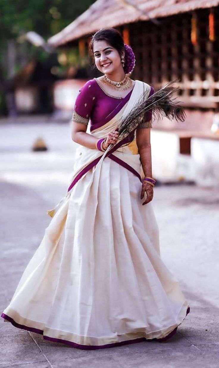 a woman in a white and purple sari with feathers on her head walking down the street