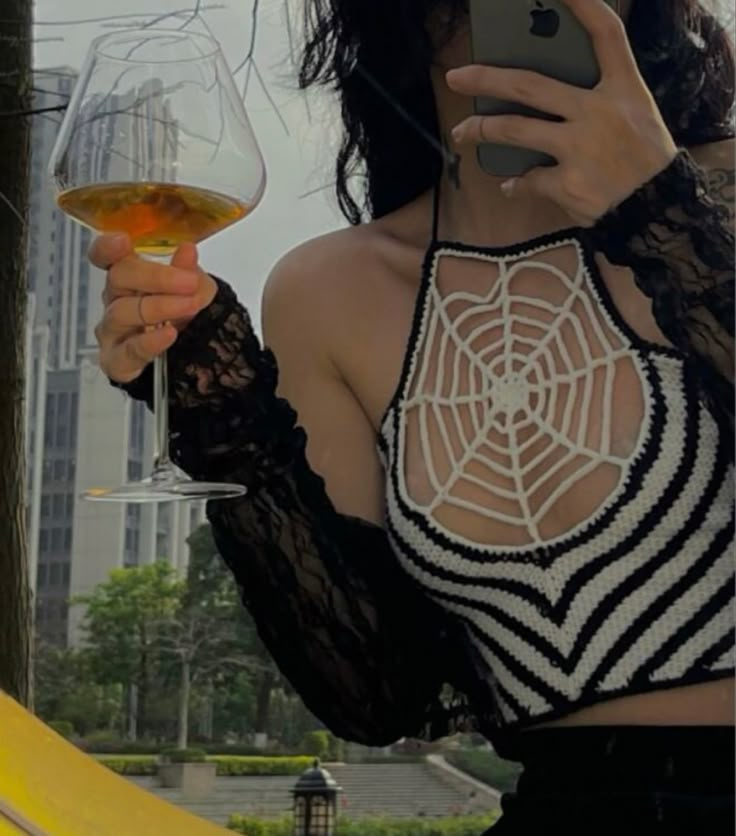 a woman holding a cell phone while wearing a black and white top with spider web on it