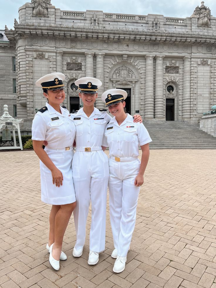 three women in white uniforms are posing for a photo outside an old building with statues behind them