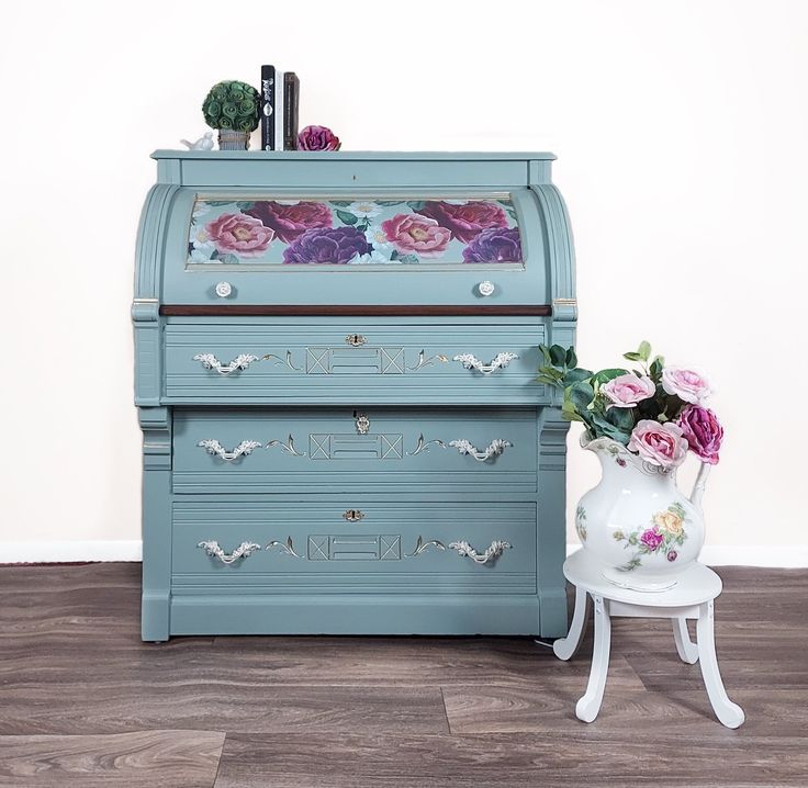 a blue dresser with flowers painted on it and a small white chair next to it