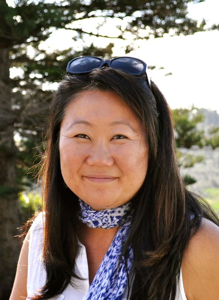 a woman with sunglasses and a scarf around her neck smiles at the camera while standing in front of a tree