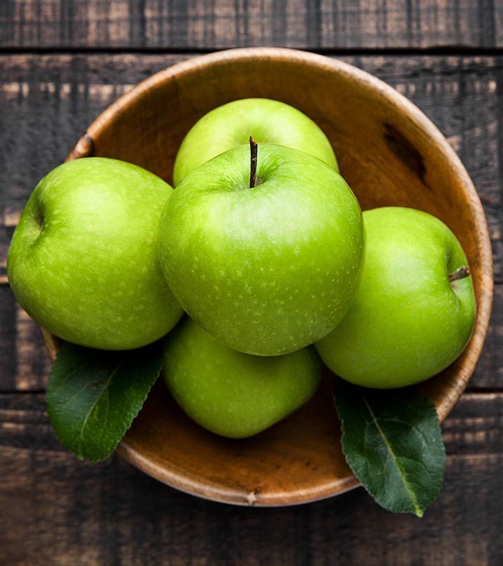 four green apples in a wooden bowl with leaves