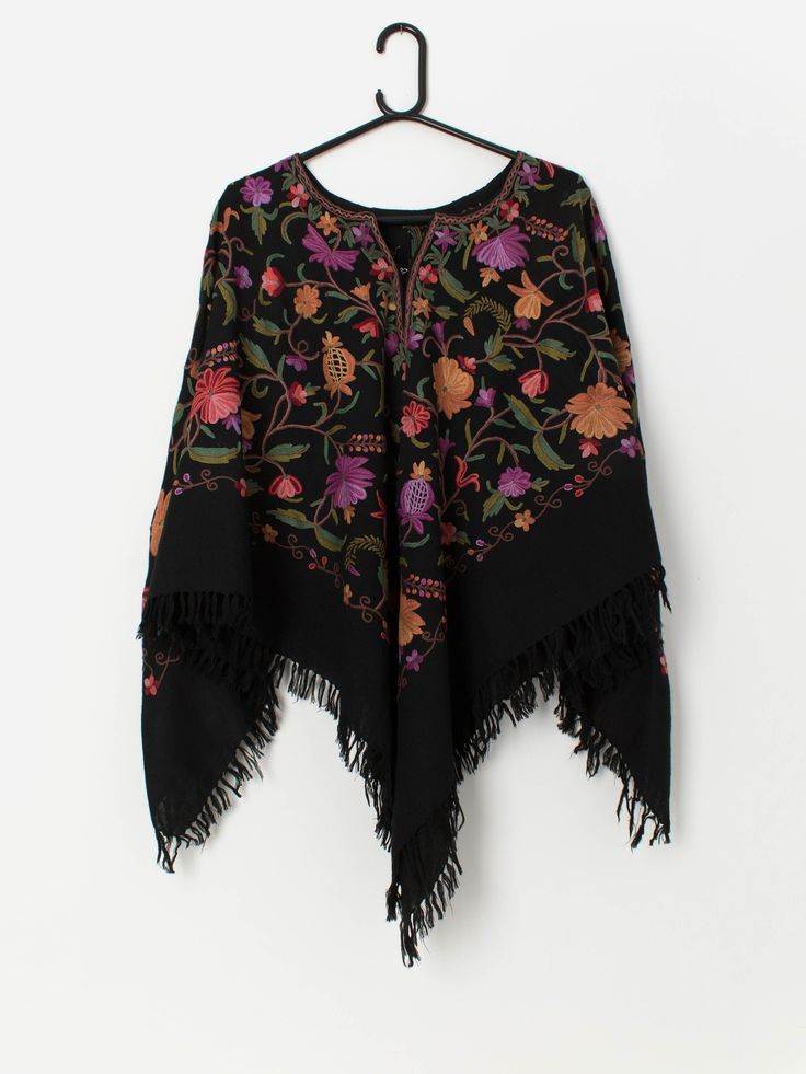 Handmade vintage black embroidered poncho with fringe detail. This 70s poncho features a gorgeous purple, red and orange embroidered floral pattern, fringe detail, a round neck and a hook and eye closure on the chest. Made from a heavyweight synthetic material. Our recommended size: One size Label says: No size label Condition: Very good Material: No care label, confident it is synthetic Measurements in inches: Shoulders: 21 Front length: 33 Back length: 31 We recommend that you compare our meas Fall Festival Poncho With Tassels, Black Fringed Shawl For Festival, Black Fringe Poncho Shawl, Bohemian Black Poncho With Tassels, Folk Style Poncho With Floral Embroidery, Black Bohemian Poncho Shawl, Winter Floral Embroidery Shawl, Festival Poncho With Multicolor Floral Embroidery, Festival Black Embroidered Poncho