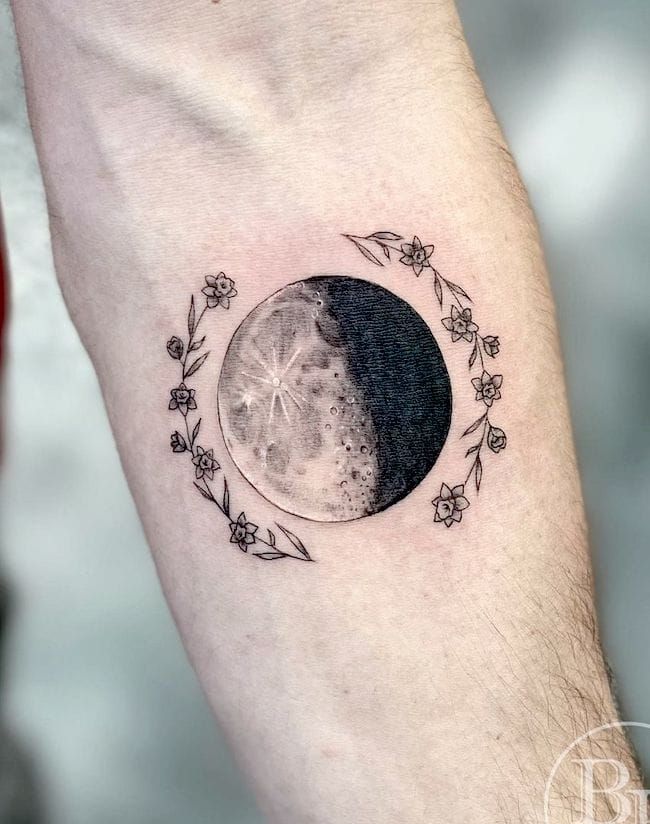 a black and white photo of a half - moon tattoo on the left arm with flowers around it