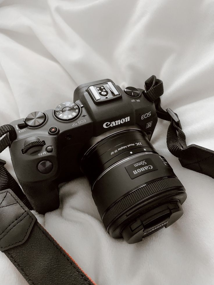 a canon camera sitting on top of a bed next to a black leather case and strap