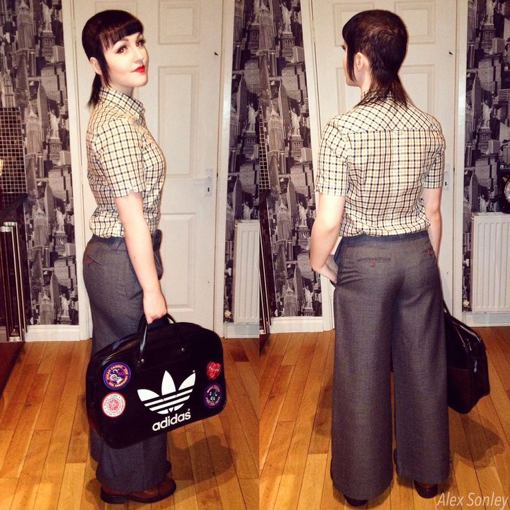 a woman standing on a hard wood floor holding a black bag and wearing grey pants