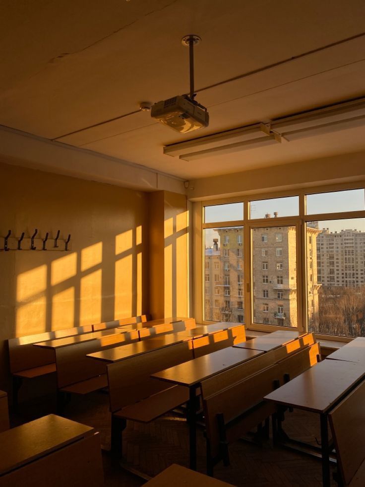 an empty classroom with desks and windows in the back ground, looking out onto city buildings