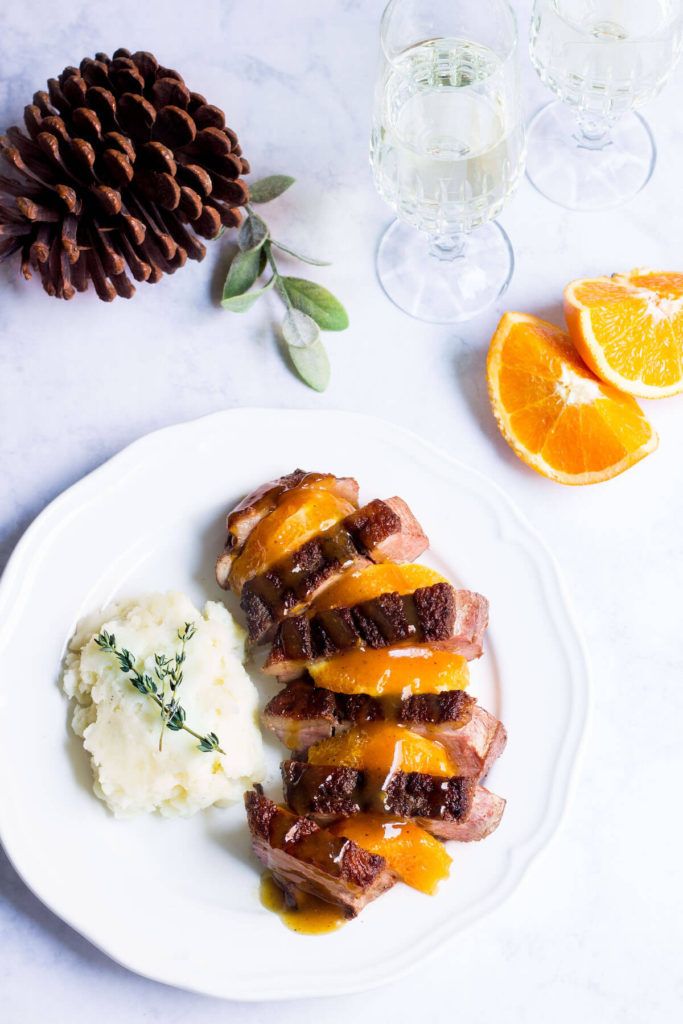 a white plate topped with meat and mashed potatoes next to an orange slice on top of a table