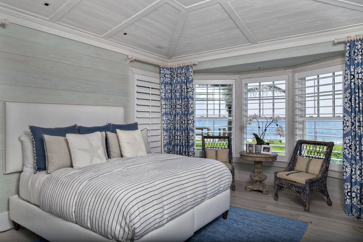 a large bed sitting in a bedroom next to a window covered in blue and white curtains