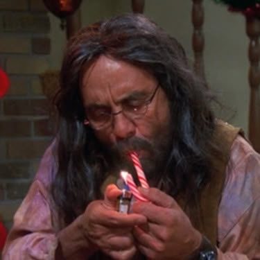 a man with long hair and glasses holding a lit candle in front of his face