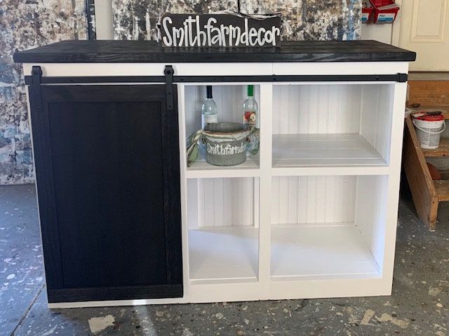 a white and black cabinet with some bottles on it's shelves in a room