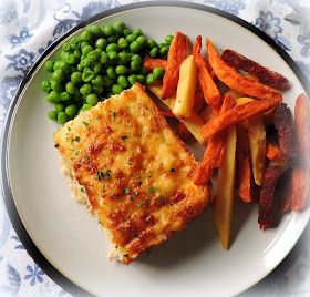 a white plate topped with fish, potatoes and green peas next to carrot wedges