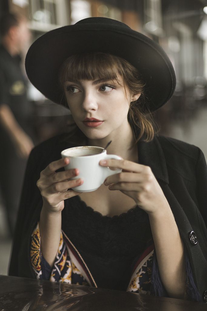 a woman wearing a black hat and holding a white coffee cup in her right hand