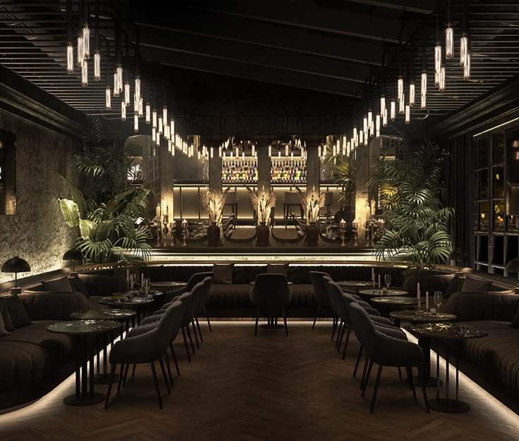 a dimly lit restaurant with long tables and chairs in front of the bar, surrounded by potted plants