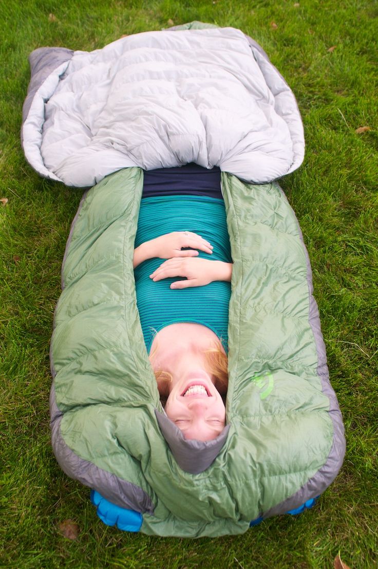 a woman laying in a sleeping bag on the grass with her head sticking out from it