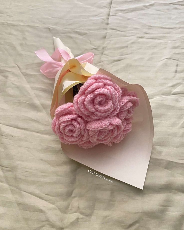 pink crocheted roses are placed in a heart shaped box on a white sheet