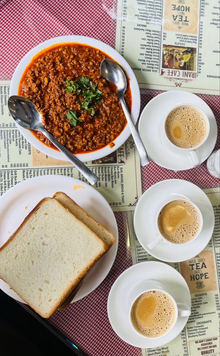 a table topped with plates of food next to cups of coffee and spoons on top of a newspaper