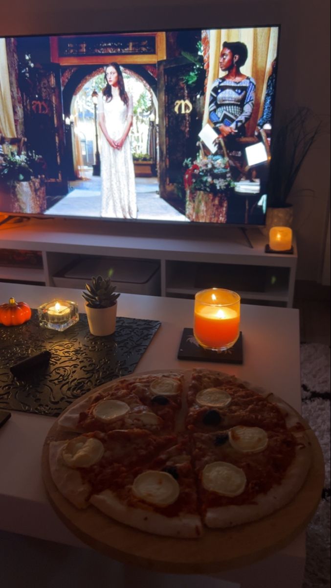 a pizza sitting on top of a table next to a flat screen tv with candles in front of it