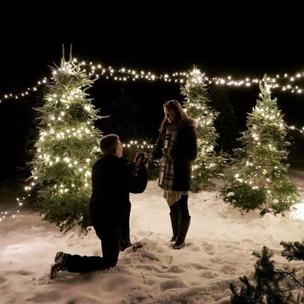 two people standing next to each other in front of christmas trees with lights on them