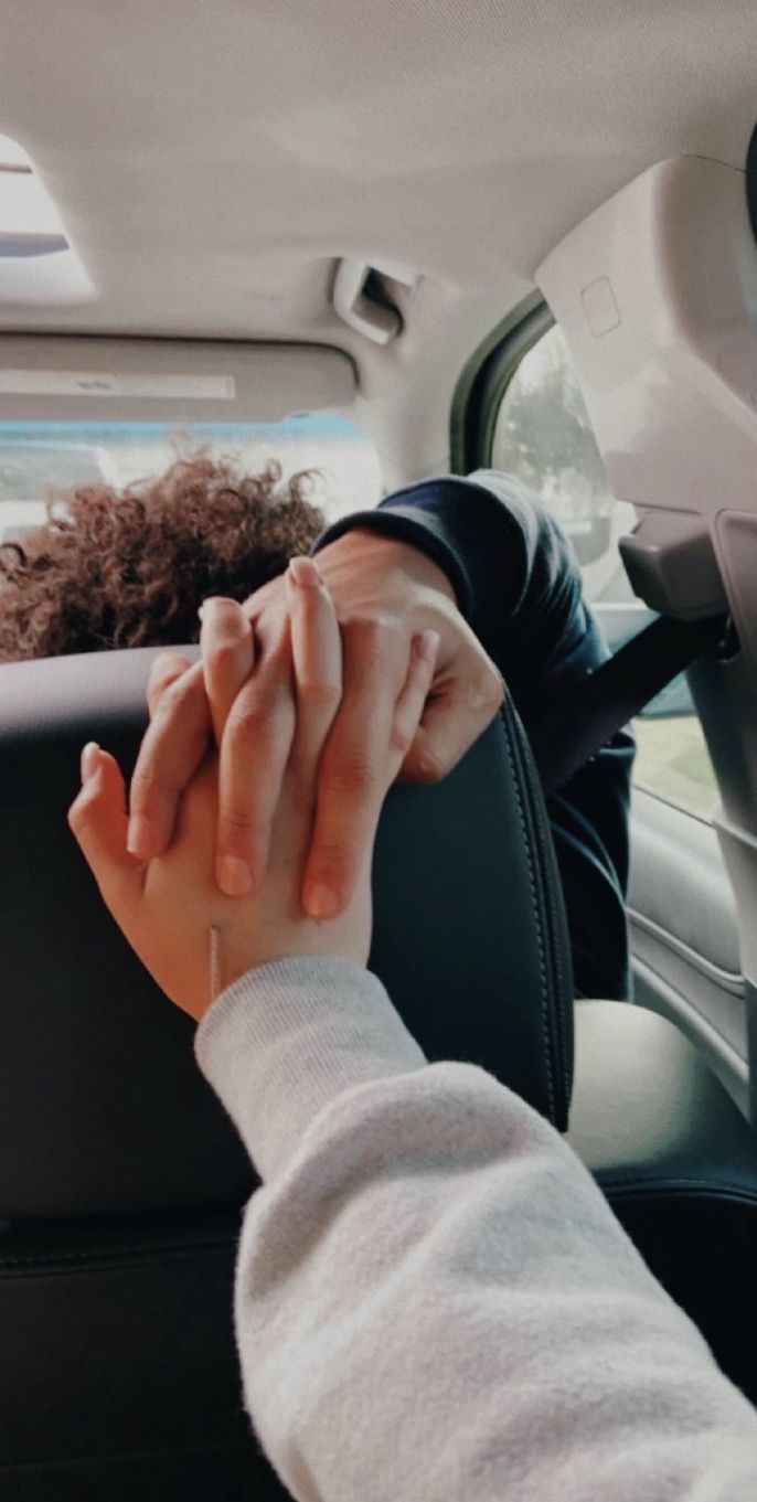 two people holding hands in the back seat of a car, one is sitting down