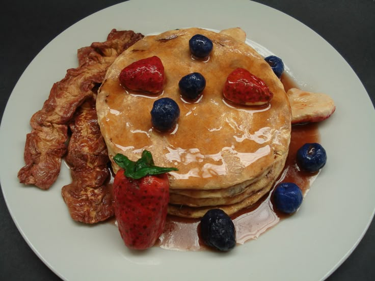 a plate with pancakes, fruit and bacon on it that is ready to be eaten