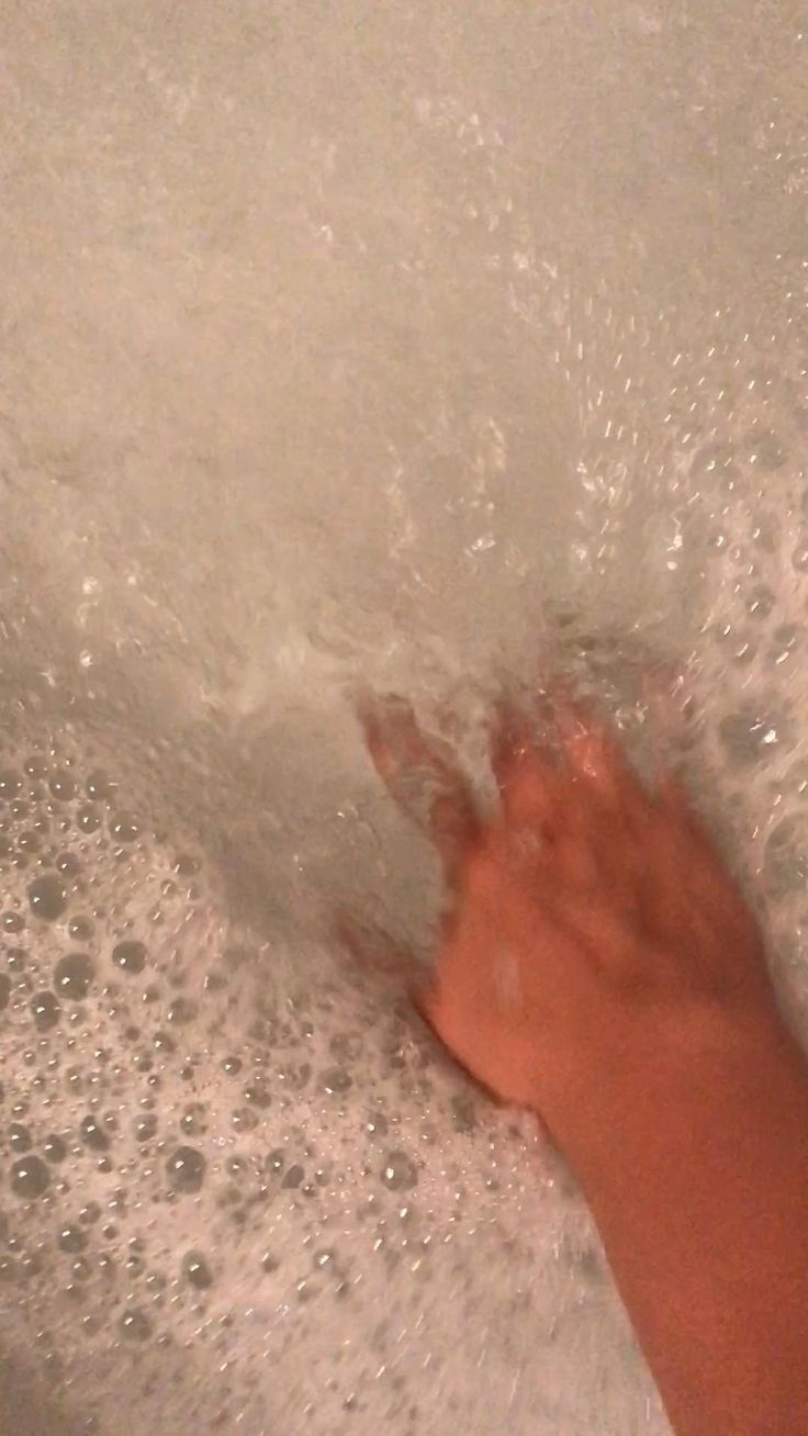 a person is washing their hands in a bathtub full of soapy water and bubbles