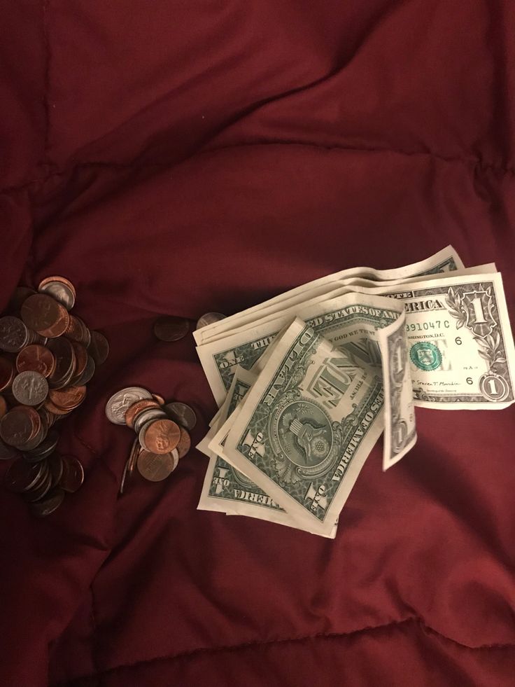 several stacks of money sitting on top of a red bed spread next to some coins