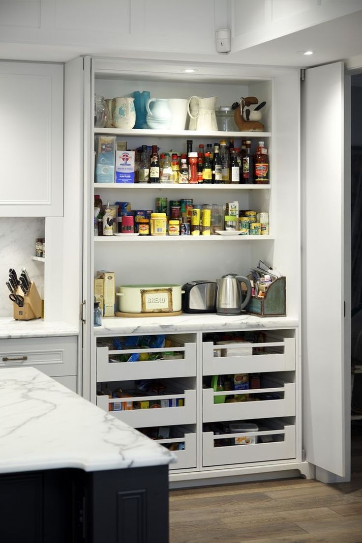 an organized pantry with white cabinets and marble counter tops in a home kitchen, showing the open shelving