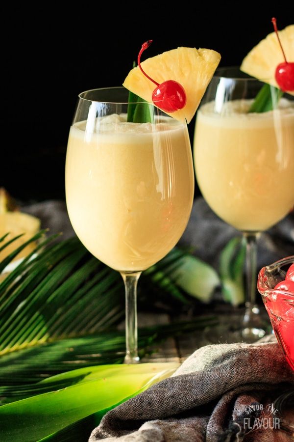 two glasses filled with drinks and garnished with pineapples on a table