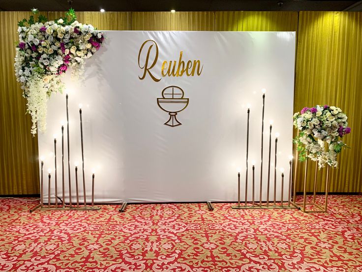 a white backdrop with flowers and candles in front of it that says reuben on the wall