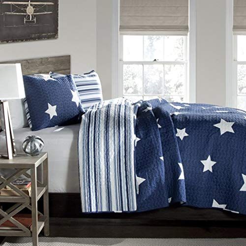 a bed with blue and white stars on it in front of a window, next to a night stand