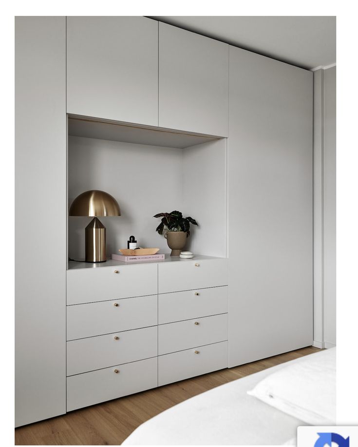 a bedroom with white cupboards and a gold lamp on the shelf next to it