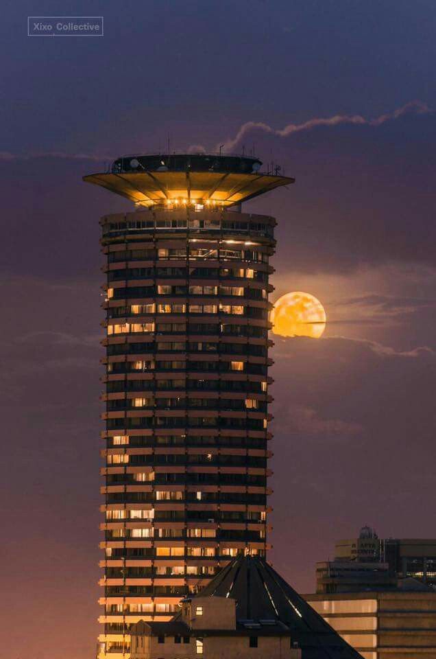 the moon is setting behind a tall building